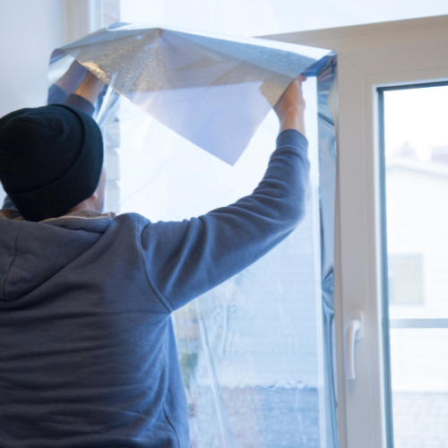 Un monsieur installe un film miroir bleu sur une porte fenêtre 