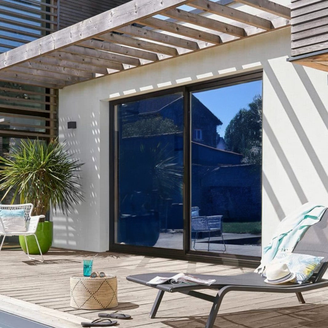 Extérieur d'une maison avec une terrasse en bois et une baie vitré avec des films miroir pour fenêtre bleu foncé