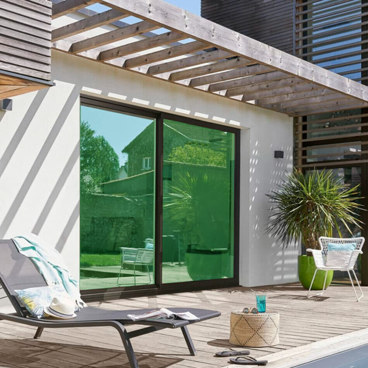 Une maison moderne avec une belle baie vitrée avec des films miroir vert donnant vue sur une belle terasse